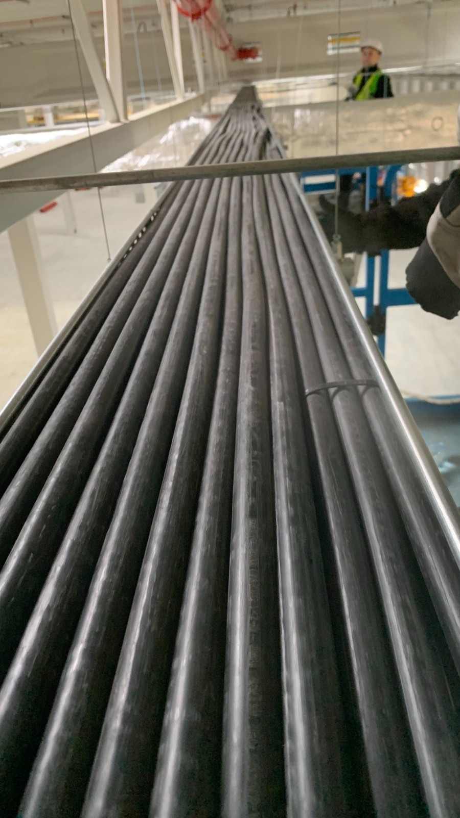 Równolegle ułożone, czarne kable elektryczne w nowym budynku, zabezpieczone opaską. W tle widoczny pracownik w kasku i kamizelce odblaskowej.