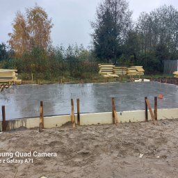 Firma budowlana Jacek Barszczewski - Świeżo wylana płyta fundamentowa z izolacją, drewniane podpory, w tle składowane materiały budowlane, jesienna aura.