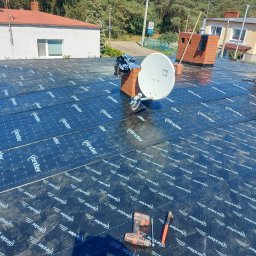 Firma budowlana Jacek Barszczewski - Dach pokryty membraną hydroizolacyjną Nexler, widoczne narzędzia (wkrętarka, nóż), antena satelitarna i kominy. Prace dekarskie w toku, widok z góry.