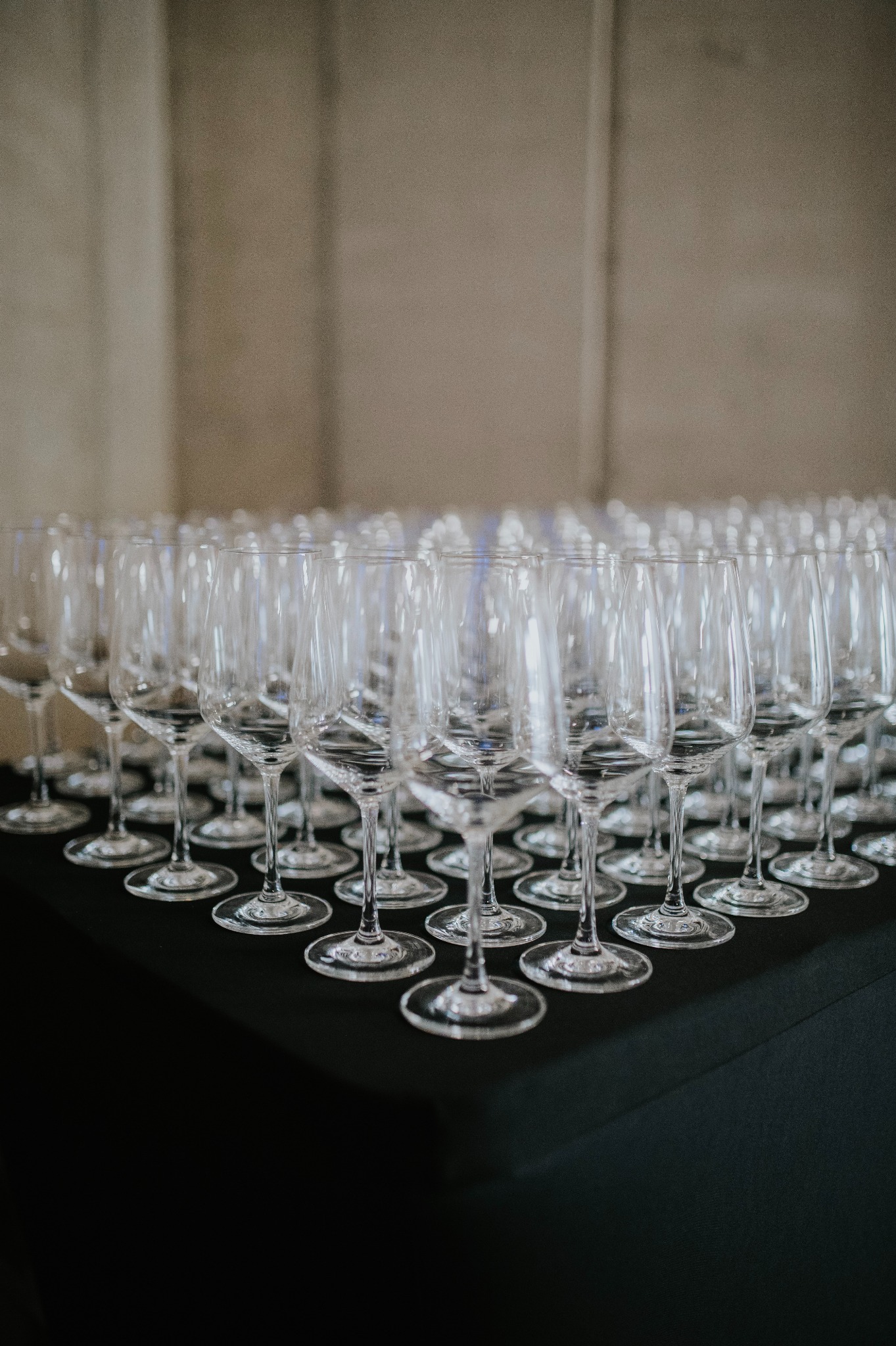 Rząd kieliszków do wina ustawionych na czarnym obrusie, gotowych do serwowania podczas eleganckiego przyjęcia. Delikatne światło podkreśla szkło.