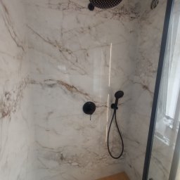 Usługi glazurnicze Wojciech Tłuchowski - Nowoczesna kabina prysznicowa z marmurowymi płytkami, deszczownicą i drewnianym brodzikiem. Czarna armatura i minimalistyczny design.