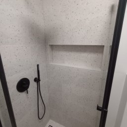 Usługi glazurnicze Wojciech Tłuchowski - Nowoczesna kabina prysznicowa z czarną armaturą i odpływem liniowym, wykończona jasnymi płytkami w drobny wzór. W ścianie wnęka.