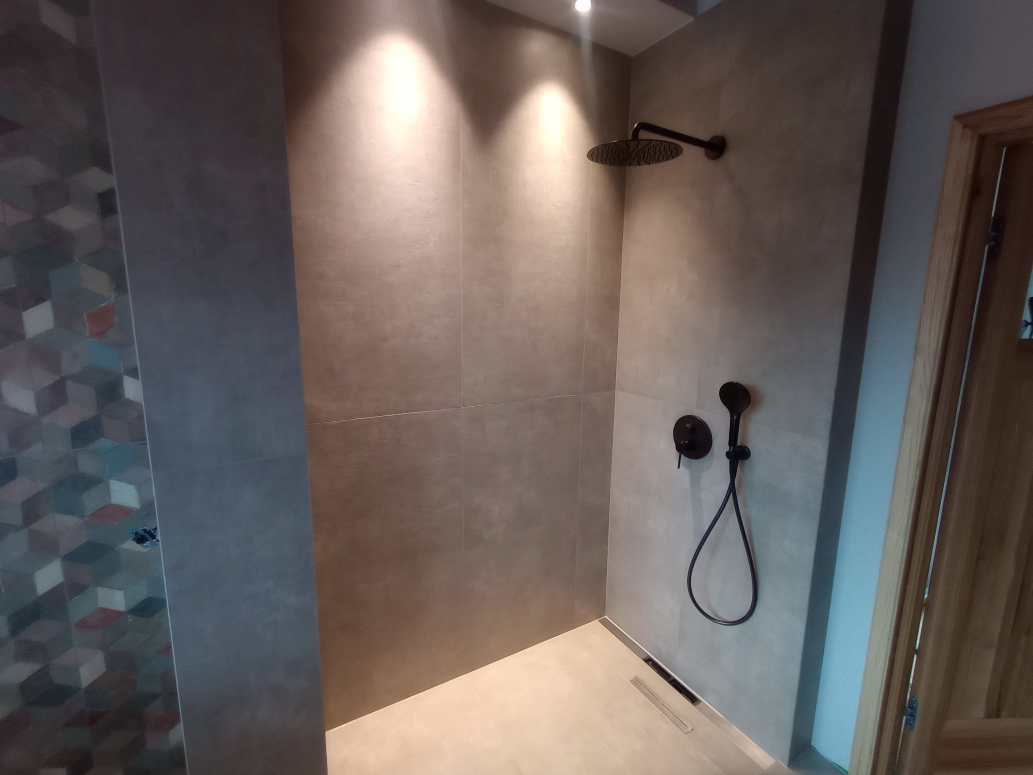 Nowoczesna kabina prysznicowa walk-in z szarymi płytkami, czarną armaturą i odpływem liniowym. Oświetlenie punktowe podkreśla minimalistyczny design.