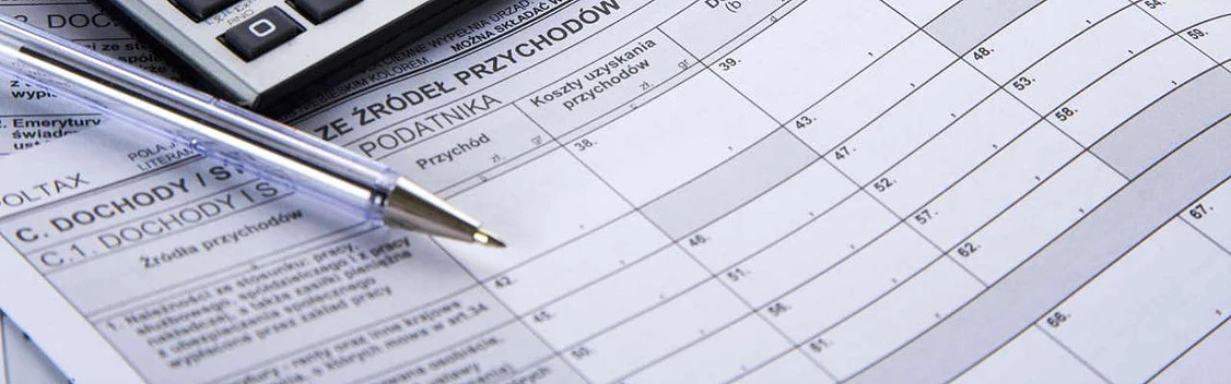 Formularz PIT z długopisem i kalkulatorem. Widoczne rubryki dotyczące przychodów i kosztów uzyskania. Dokumenty finansowe w biurze rachunkowym.