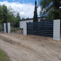 JARCZAR - Nowoczesna, pozioma brama wjazdowa z szarego metalu, osadzona na betonowych słupkach. W tle dom jednorodzinny i fragment ogrodzenia panelowego.