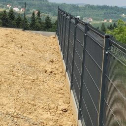 JARCZAR - Nowoczesne, grafitowe ogrodzenie panelowe na betonowej podmurówce, z widokiem na pagórkowaty krajobraz w tle. Ujęcie z bliska, podkreślające detale konstrukcji.