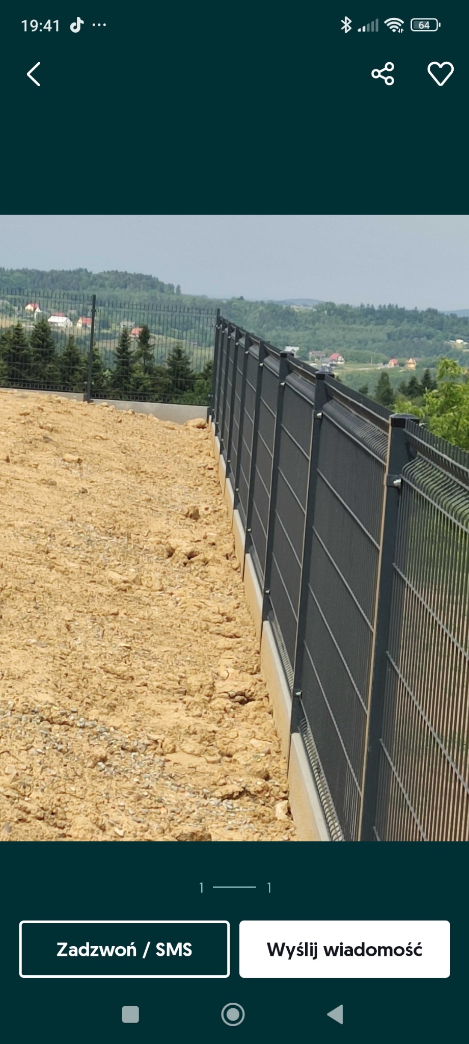 Nowoczesne, grafitowe ogrodzenie panelowe na betonowej podmurówce, z widokiem na pagórkowaty krajobraz w tle. Ujęcie z bliska, podkreślające detale konstrukcji.