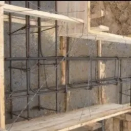 Zbrojenie fundamentu w drewnianym szalunku, widoczne pręty zbrojeniowe połączone drutem, przygotowane do zalania betonem. Widok z góry.