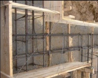 Zbrojenie fundamentu w drewnianym szalunku, widoczne pręty zbrojeniowe połączone drutem, przygotowane do zalania betonem. Widok z góry.