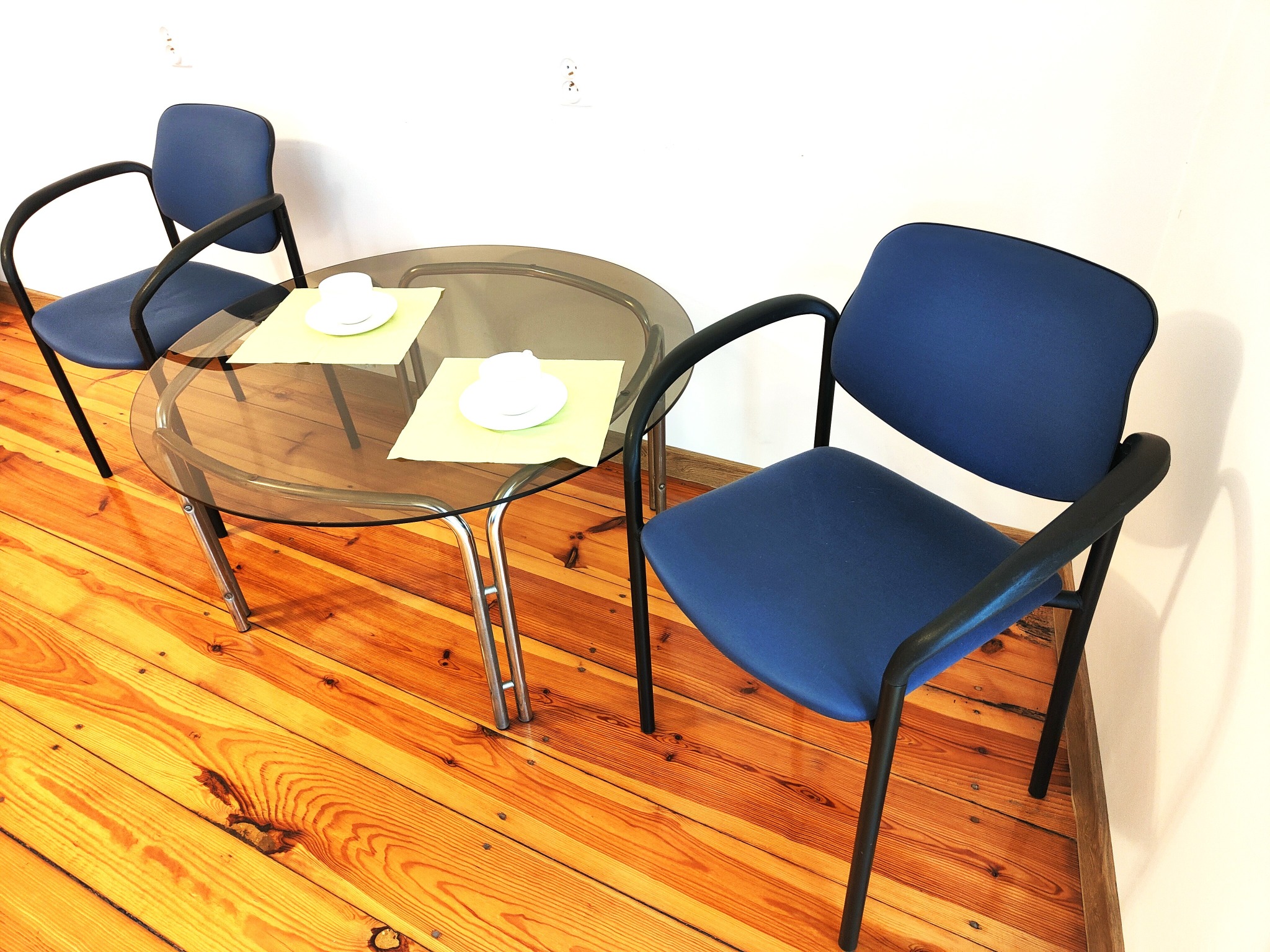 Dwa krzesła przy szklanym stoliku z filiżankami na drewnianej podłodze. Jasne wnętrze, minimalistyczny wystrój. Widok z góry, oświetlenie naturalne.