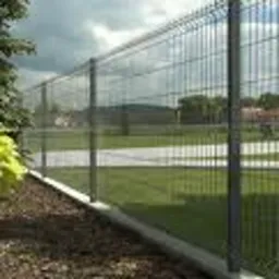 Nowoczesne ogrodzenie panelowe zgrzewane, osadzone na betonowej podmurówce, widoczne na tle zielonego trawnika i pochmurnego nieba.