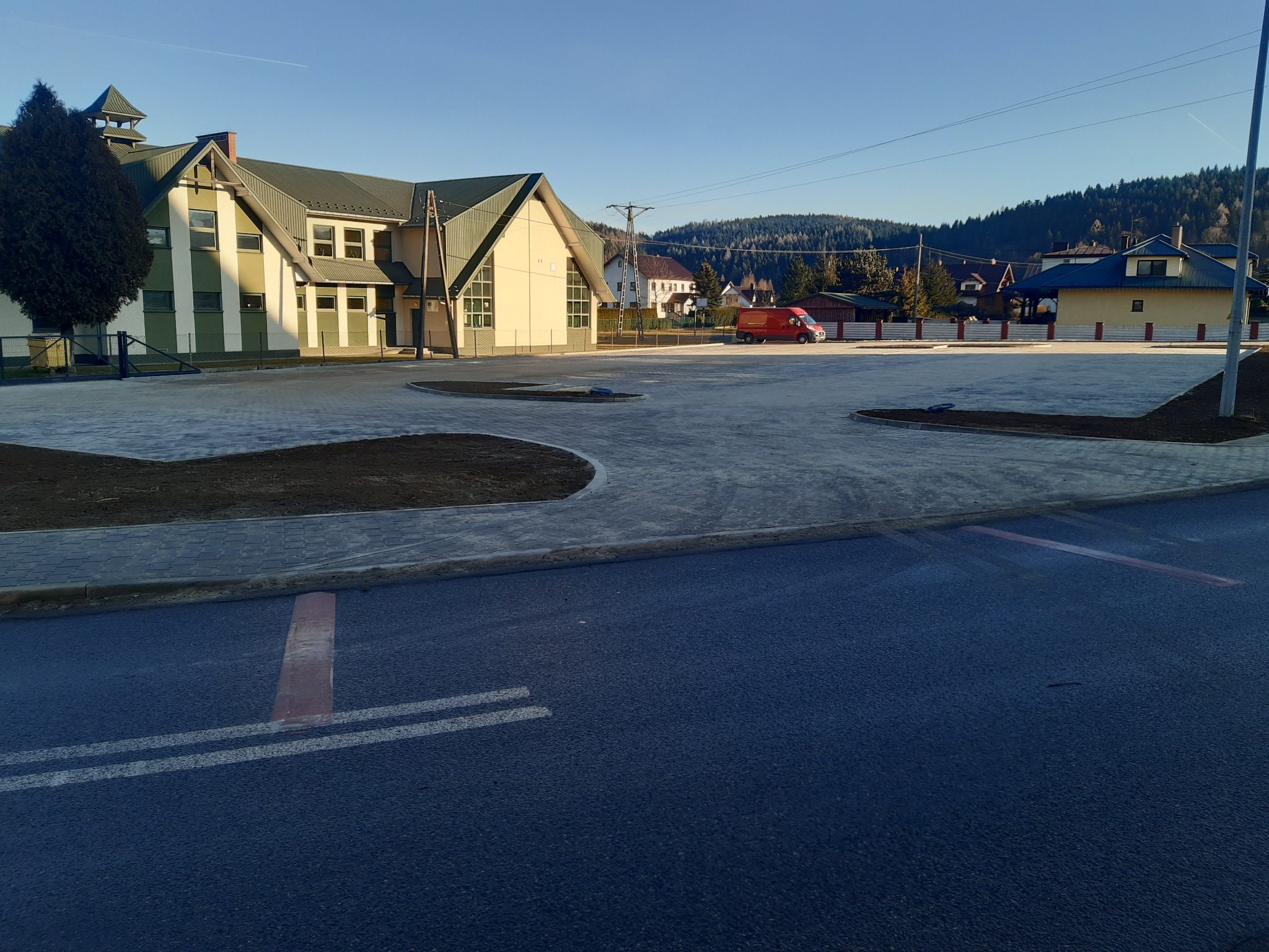 Nowa nawierzchnia z kostki brukowej przed budynkiem w górskim krajobrazie, świeżo ułożona ziemia, widok na góry w tle, słoneczny dzień.