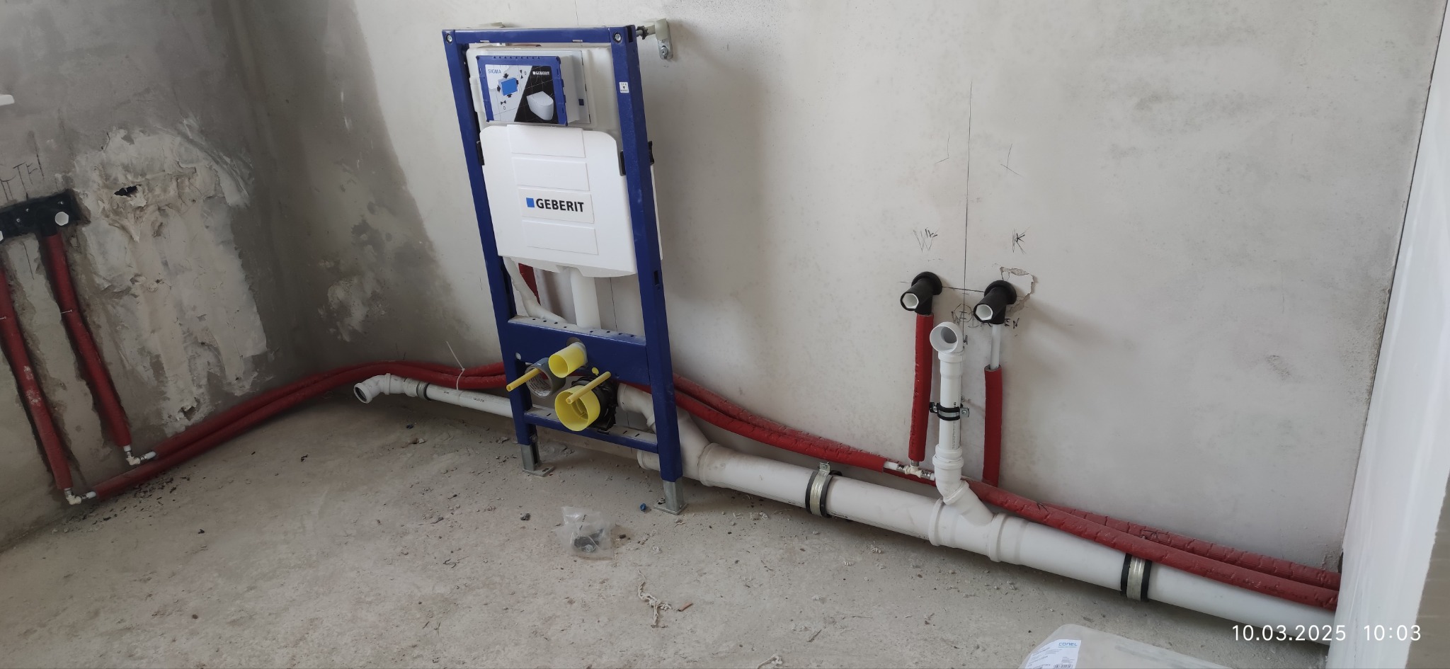 Montaż podtynkowego stelaża WC Geberit z instalacją hydrauliczną w surowym stanie, widoczne rury doprowadzające wodę i odpływ. Ściany w trakcie wykończenia.