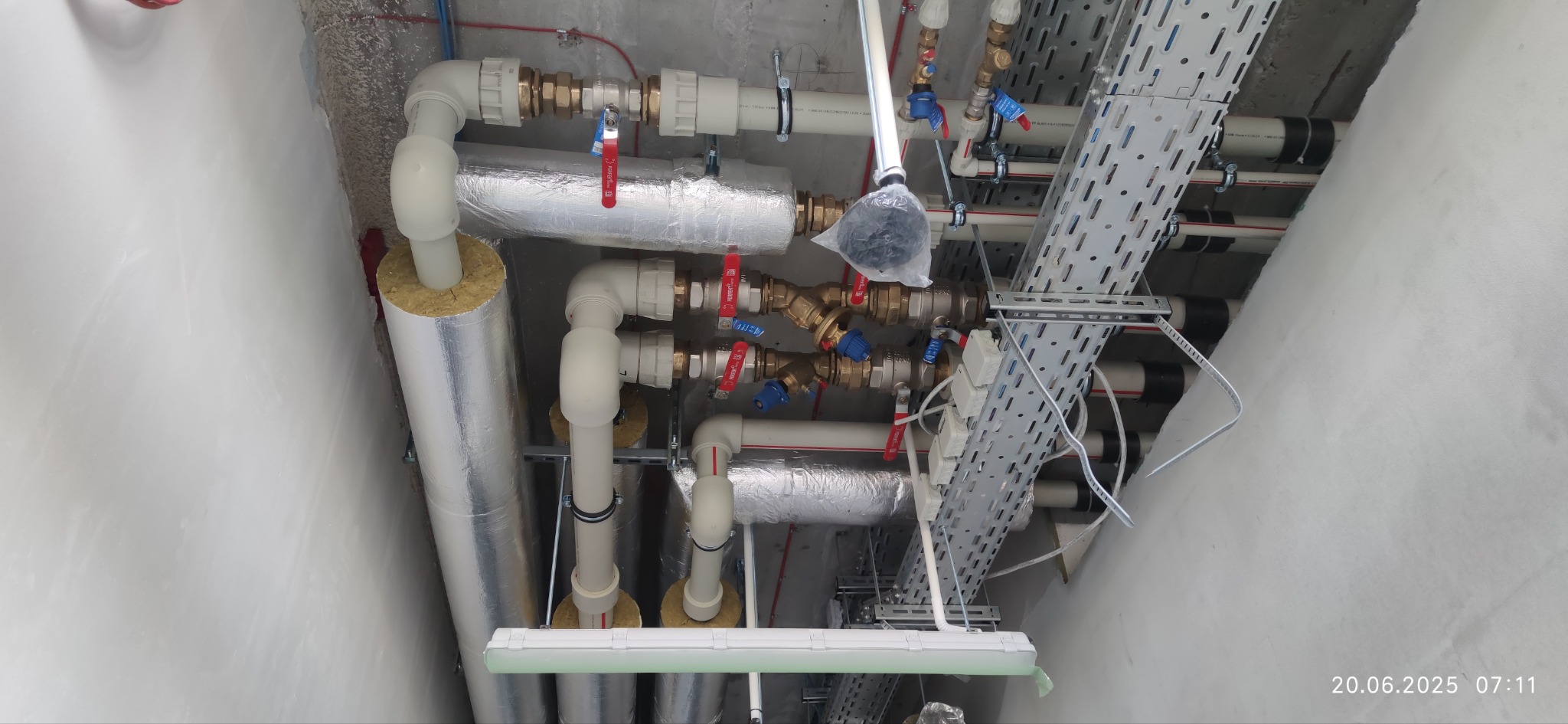 Instalacja rur z zaworami i izolacją termiczną, widok z dołu. Szyny montażowe. Elementy instalacji hydraulicznej i wentylacyjnej pod sufitem w surowym stanie.