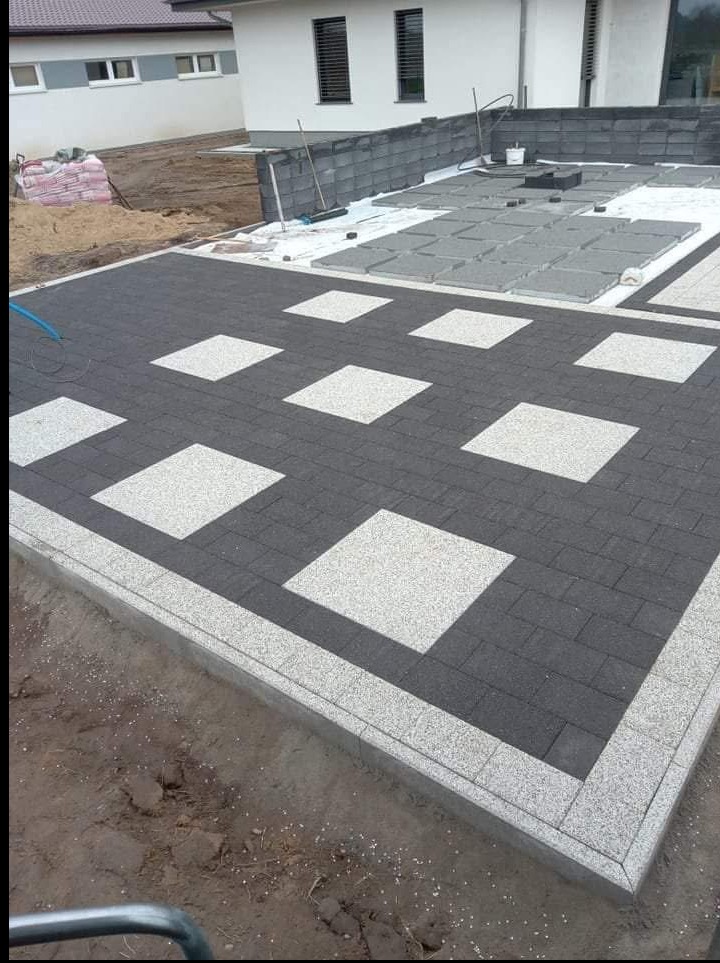 Nowoczesna aranżacja z kostki brukowej: ciemnoszare prostokąty i jasne kwadraty, obrzeże z szarego grysu. Częściowo ułożona powierzchnia z przygotowanymi materiałami.