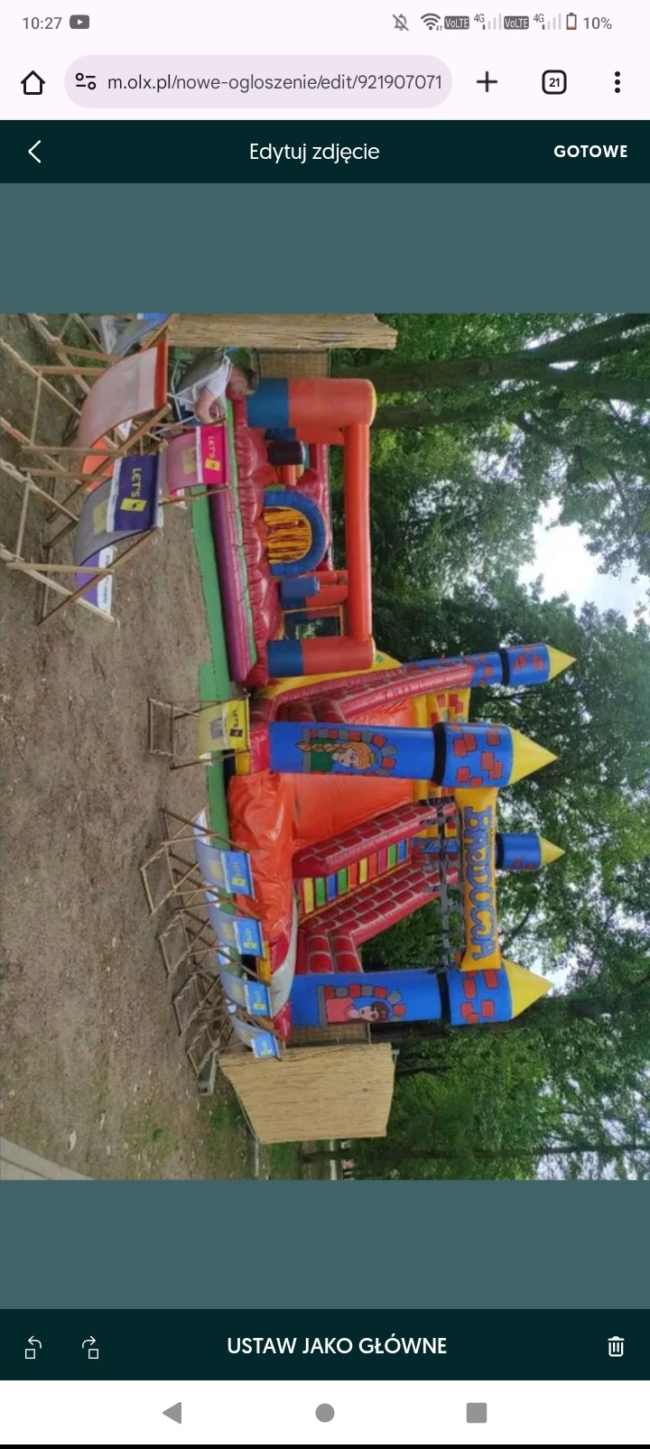 Kolorowy, rozłożony dmuchany zamek z motywami bajkowymi na trawiastym terenie, widziany z boku, z widocznymi krzesłami i fragmentem drzewa w tle. Zestaw 1.