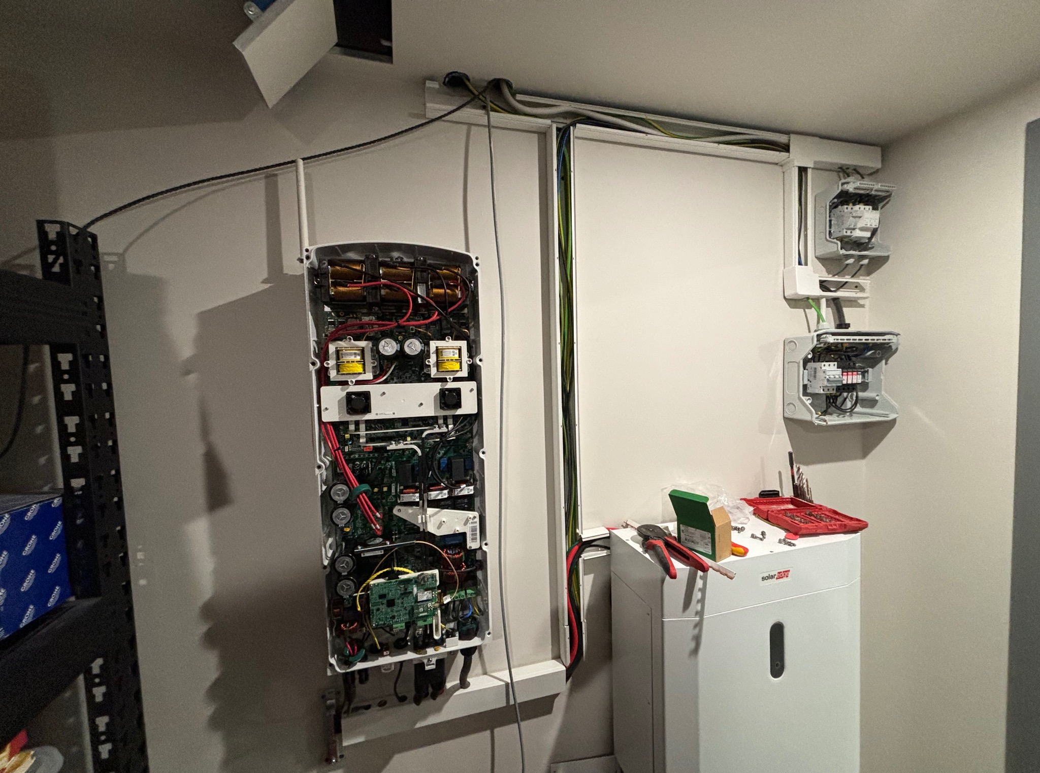 Otwarta obudowa falownika SolarEdge z widocznymi komponentami elektronicznymi, narzędzia obok, kable prowadzone w listwach. Montaż instalacji fotowoltaicznej.