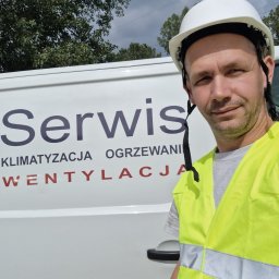 Serhii Cholavyn - Pracownik serwisu klimatyzacji, ogrzewania i wentylacji w kamizelce odblaskowej i kasku na tle firmowego samochodu w Warszawie. Widoczne logo firmy.