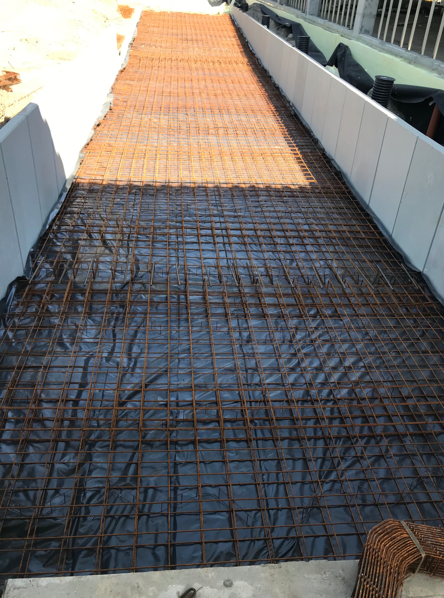 Przygotowany szkielet zbrojenia na czarnej folii, gotowy do zalania betonem. Widoczne elementy szalunku i wystające pręty zbrojeniowe.