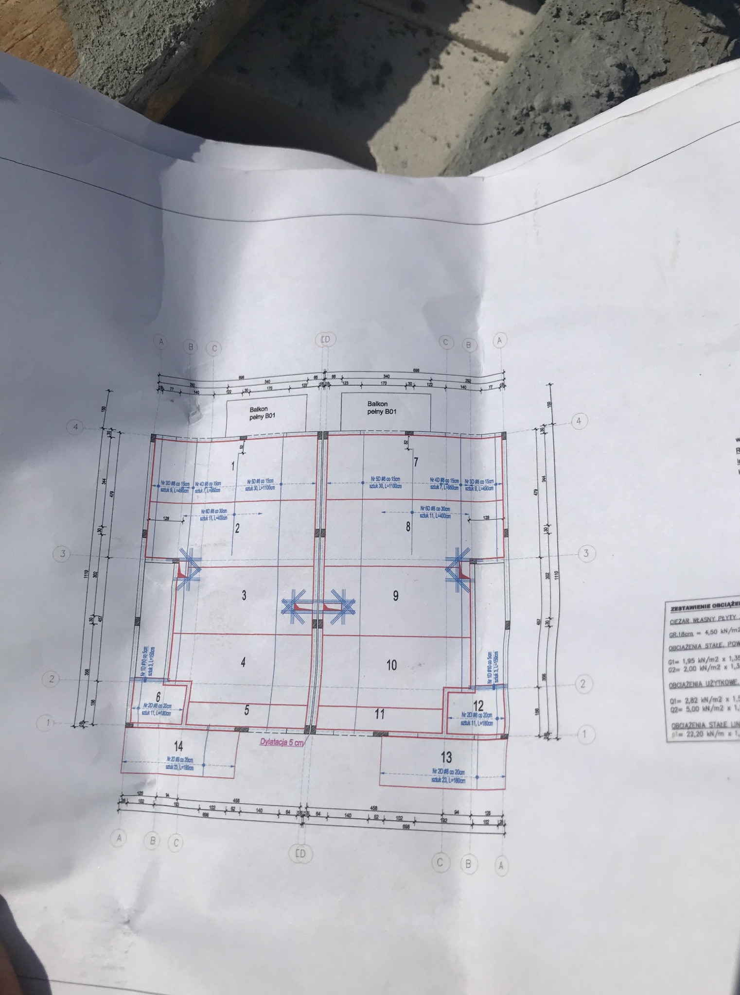 Plan konstrukcyjny balkonu w Bydgoszczy z detalami zbrojenia i wymiarami, leżący na surowym betonie. Widoczne oznaczenia i obliczenia obciążeń.