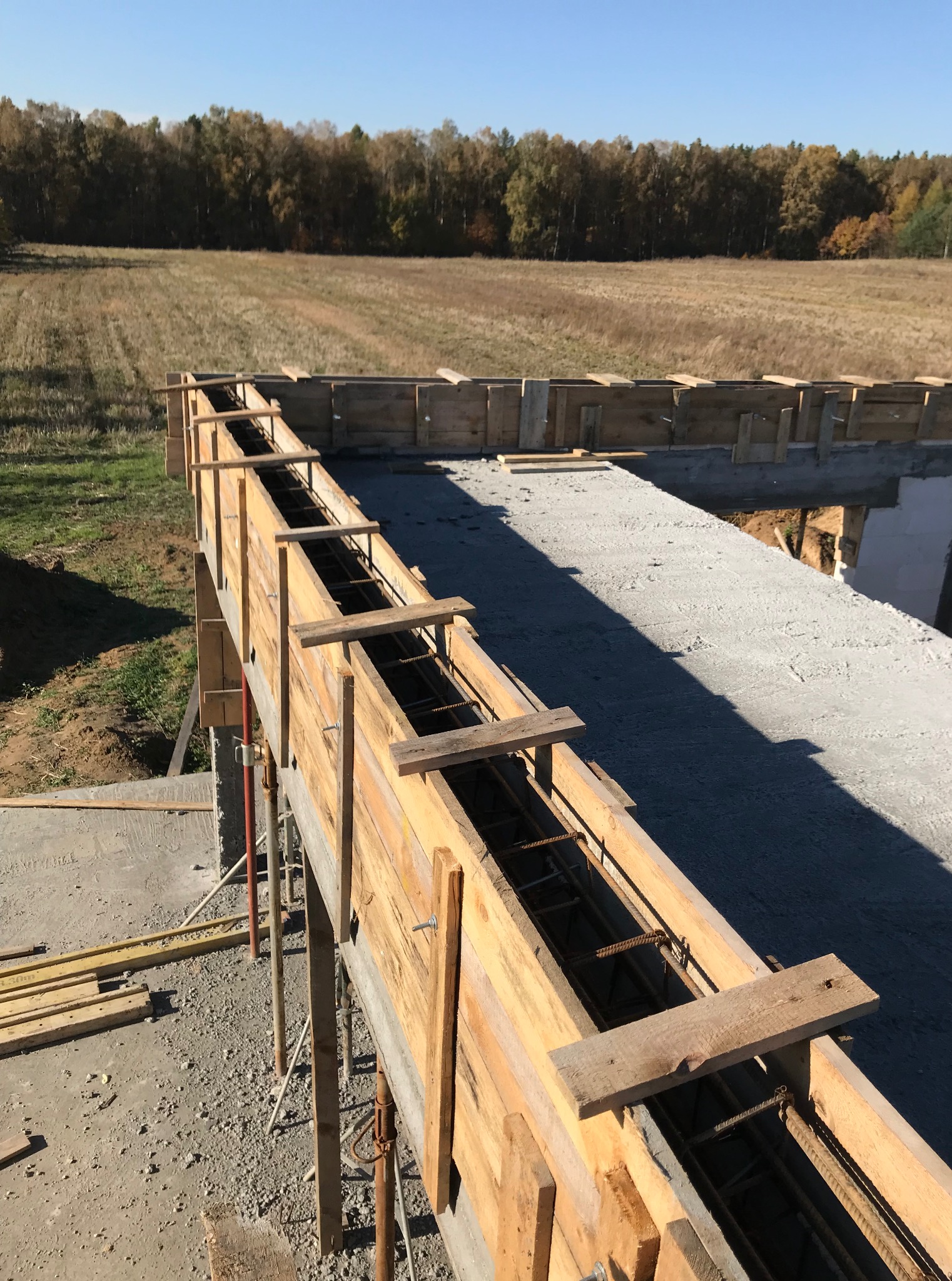 Szczegółowy widok szalunku zbrojeniowego z widoczną stalą zbrojeniową, przygotowanego do zalania betonem na tle pola i lasu.