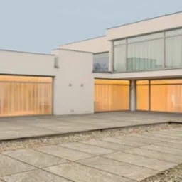 Nowoczesny dom z dużymi oknami i tarasem wyłożonym płytami w odcieniach beżu. Widoczne zasłony w oknach i żwirowe rabaty.