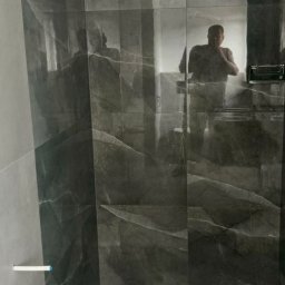 Oleksandr Mykharskyi - Elegancka łazienka z szarymi płytkami imitującymi marmur, widoczny odpływ liniowy i oświetlenie sufitowe. W lustrze odbija się osoba robiąca zdjęcie.