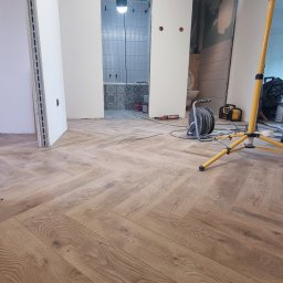 Oleksandr Mykharskyi - Parkiet ułożony w jodełkę na podłodze w trakcie remontu. W tle widoczna łazienka w trakcie wykończenia, z położonymi płytkami. Na podłodze leżą narzędzia.