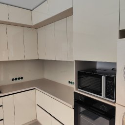 Oleksandr Mykharskyi - Beżowa, narożna zabudowa kuchenna z piekarnikiem i mikrofalówką w nowoczesnym stylu. Widoczne gniazdka elektryczne w ścianie nad blatem.