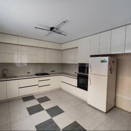 Oleksandr Mykharskyi - Jasna kuchnia z błyszczącymi frontami, czarnymi uchwytami i szachownicą na podłodze. Widoczny fragment ściany przed wykończeniem obok lodówki.