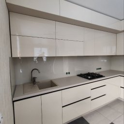 Oleksandr Mykharskyi - Nowoczesna, jasna kuchnia z błyszczącymi frontami szafek, szarym blatem i płytkami podłogowymi w szachownicę. Minimalistyczny design z widoczną płytą grzewczą i zlewem.