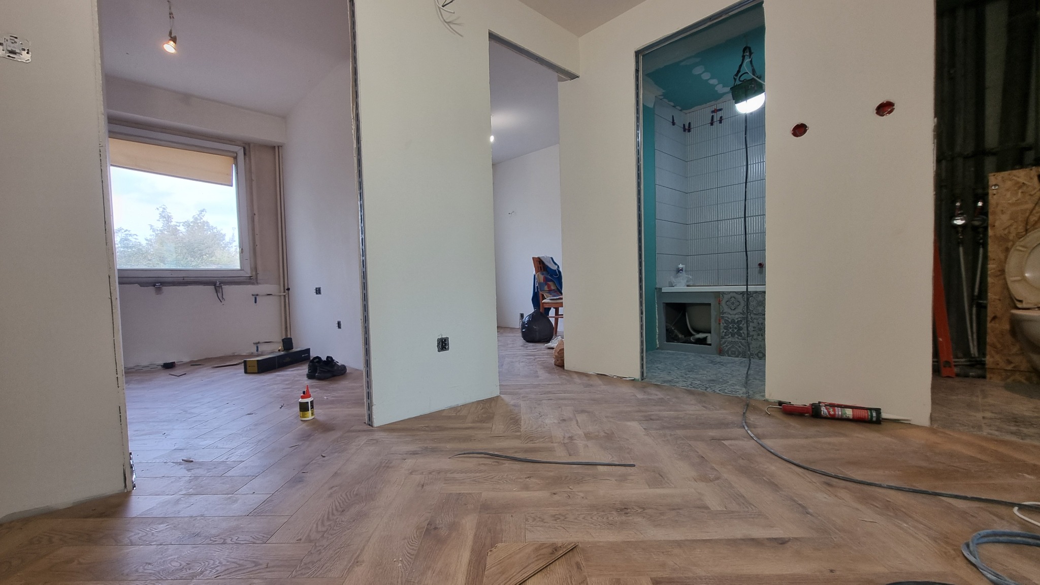 Wnętrze w trakcie prac wykończeniowych: ułożona podłoga z paneli, widoczna łazienka z płytkami, przygotowane ściany do malowania, narzędzia pracy. Wnętrze w stylu skandynawskim.