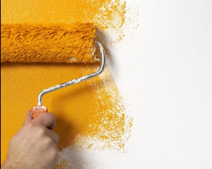 Malowanie ściany wałkiem na złoto. Dłoń trzyma narzędzie, widoczny fragment pomalowanej i surowej ściany. Tekstura farby i wałka.