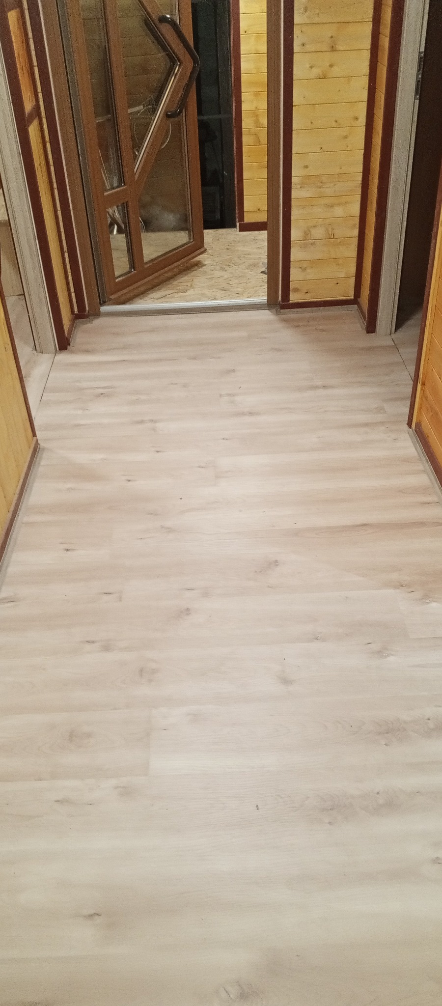 Jasne panele podłogowe ułożone w nowym wnętrzu z drewnianymi ścianami i oknami. Widok z góry na podłogę w trakcie wykańczania pomieszczenia.