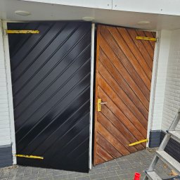 Usługi Wykończeniowo- Remontowe Robi-Bobi Robert Orzłowski - Drewniane drzwi z ukośnymi panelami, jedna część pomalowana na czarno z połyskiem, druga w naturalnym odcieniu drewna. Widoczne akcesoria malarskie i drabina.