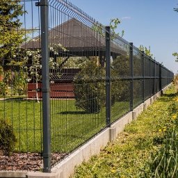 Montaz ogrodzeń Tomasz Gutowski - Grafitowe ogrodzenie panelowe na betonowej podmurówce, z widoczną altaną w tle, otoczone zielenią. Słoneczny dzień, wyraźny kadr.