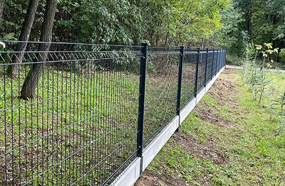 Nowoczesne ogrodzenie panelowe z podmurówką betonową, widoczne na tle zieleni. Ciemnoszary panel zgrzewany, równomiernie rozciągnięty wzdłuż działki.