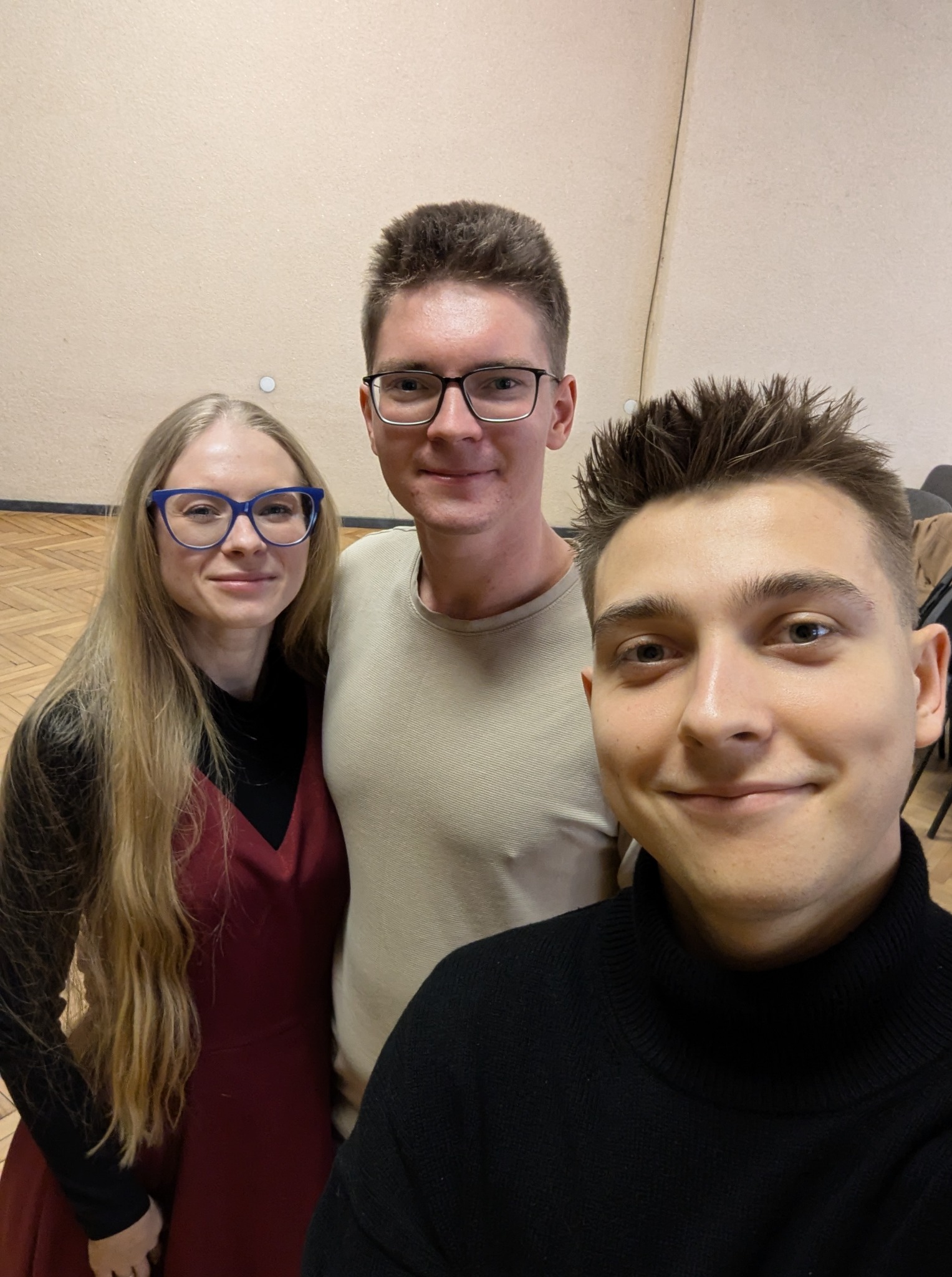 Trzy uśmiechnięte osoby, w tym potencjalny instruktor z przodu, pozują do selfie w sali z drewnianą podłogą, sugerując atmosferę szkoły tańca.