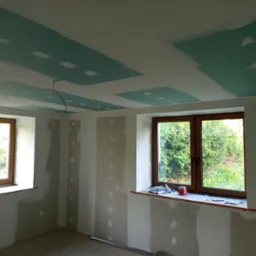 Wnętrze w trakcie prac w Gorzanowie: ściany przygotowane do malowania, częściowo położona płyta karton-gips na suficie z widocznymi łączeniami. Dwa okna z drewnianą stolarką.