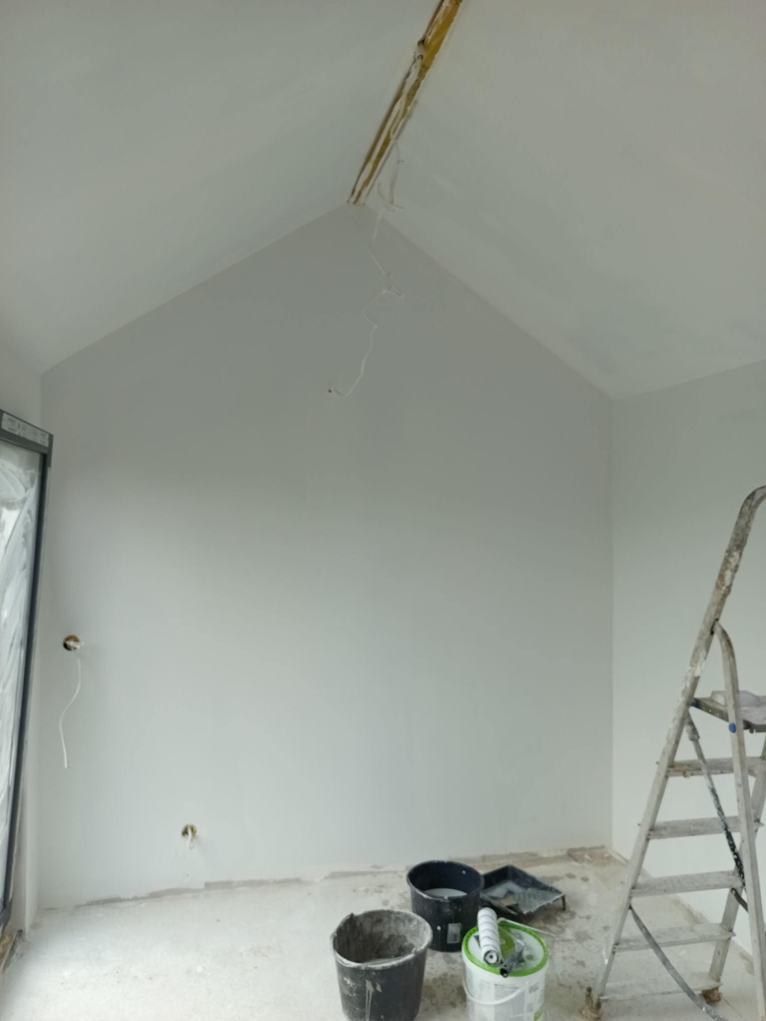 Wnętrze w trakcie malowania: białe ściany, drabina, wiaderka z farbą i wałki malarskie. Widoczne niedokończone prace przy suficie i wystające przewody.