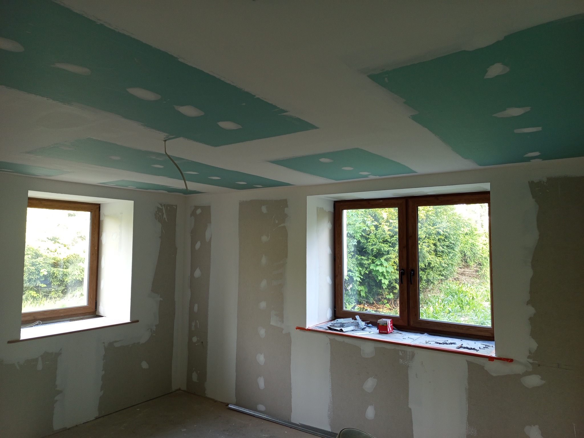 Wnętrze w trakcie prac w Gorzanowie: ściany przygotowane do malowania, częściowo położona płyta karton-gips na suficie z widocznymi łączeniami. Dwa okna z drewnianą stolarką.