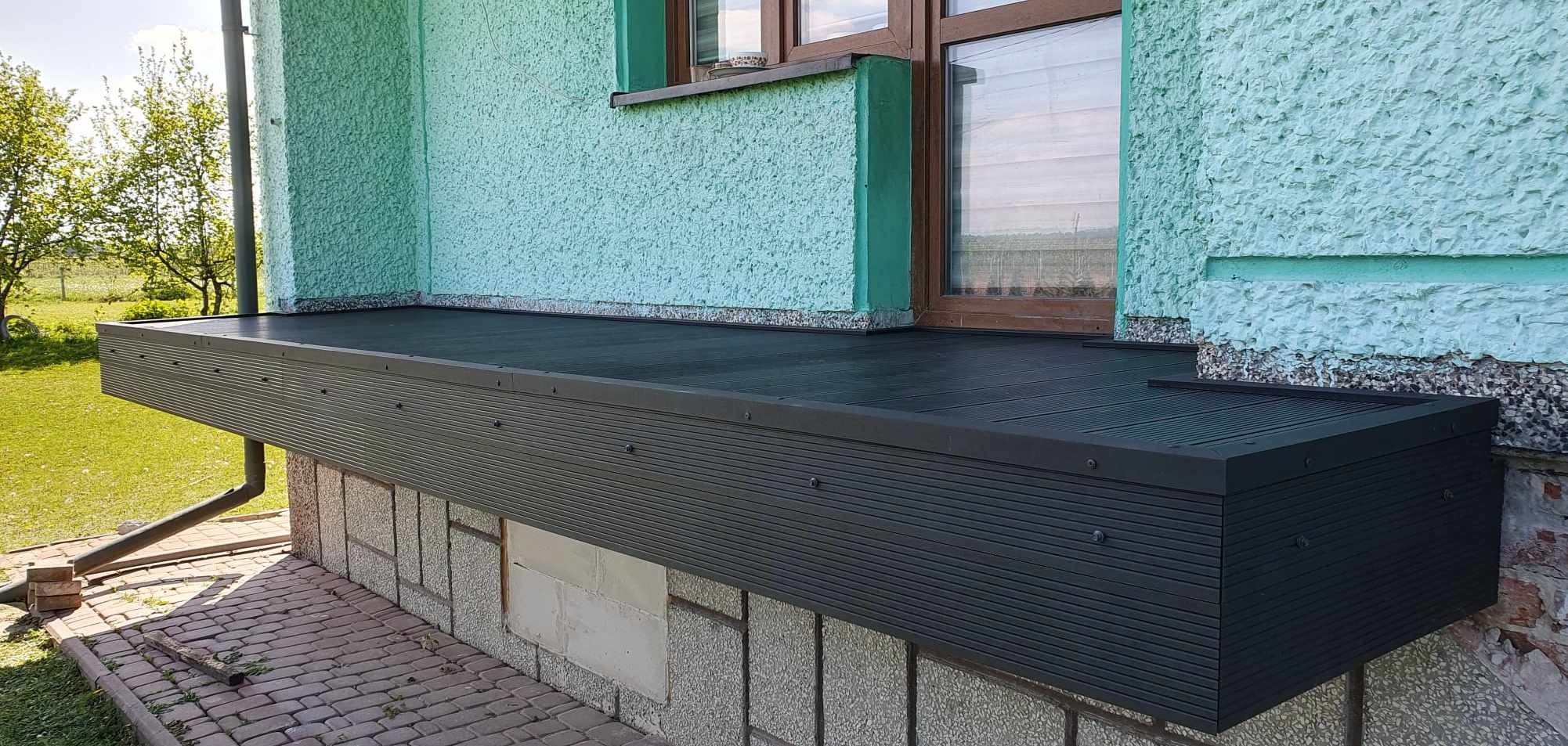 Zmodernizowany balkon z ciemną, kompozytową deską, przymocowany do turkusowej ściany budynku. Widoczne detale montażu i faktura elewacji.