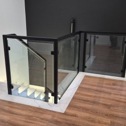 AJ.MOBISPAW - Szklana balustrada z czarną ramą, zabezpieczająca schody z podświetleniem LED. Nowoczesny design z marmurowym wykończeniem podłogi i kontrastującą czarną ścianą.