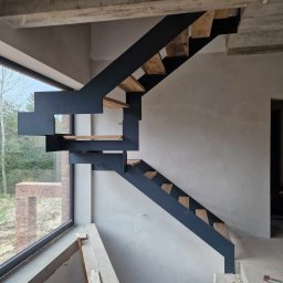 AJ.MOBISPAW - Nowoczesne schody metalowe z drewnianymi stopniami, w surowym wnętrzu budynku w trakcie budowy, z dużym oknem w tle.