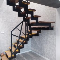 AJ.MOBISPAW - Nowoczesne schody metalowe z drewnianymi stopniami, zabezpieczone taśmą malarską. Minimalistyczny design, szara ściana i podłoga, widok z dołu na konstrukcję.