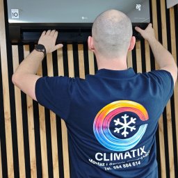 Climatix - Przegląd klimatyzacji LG Dual Inverter na ścianie z drewnianymi panelami. Mężczyzna w koszulce firmowej ClimatiX wykonuje serwis. Widoczny wyświetlacz z temperaturą 22°C.