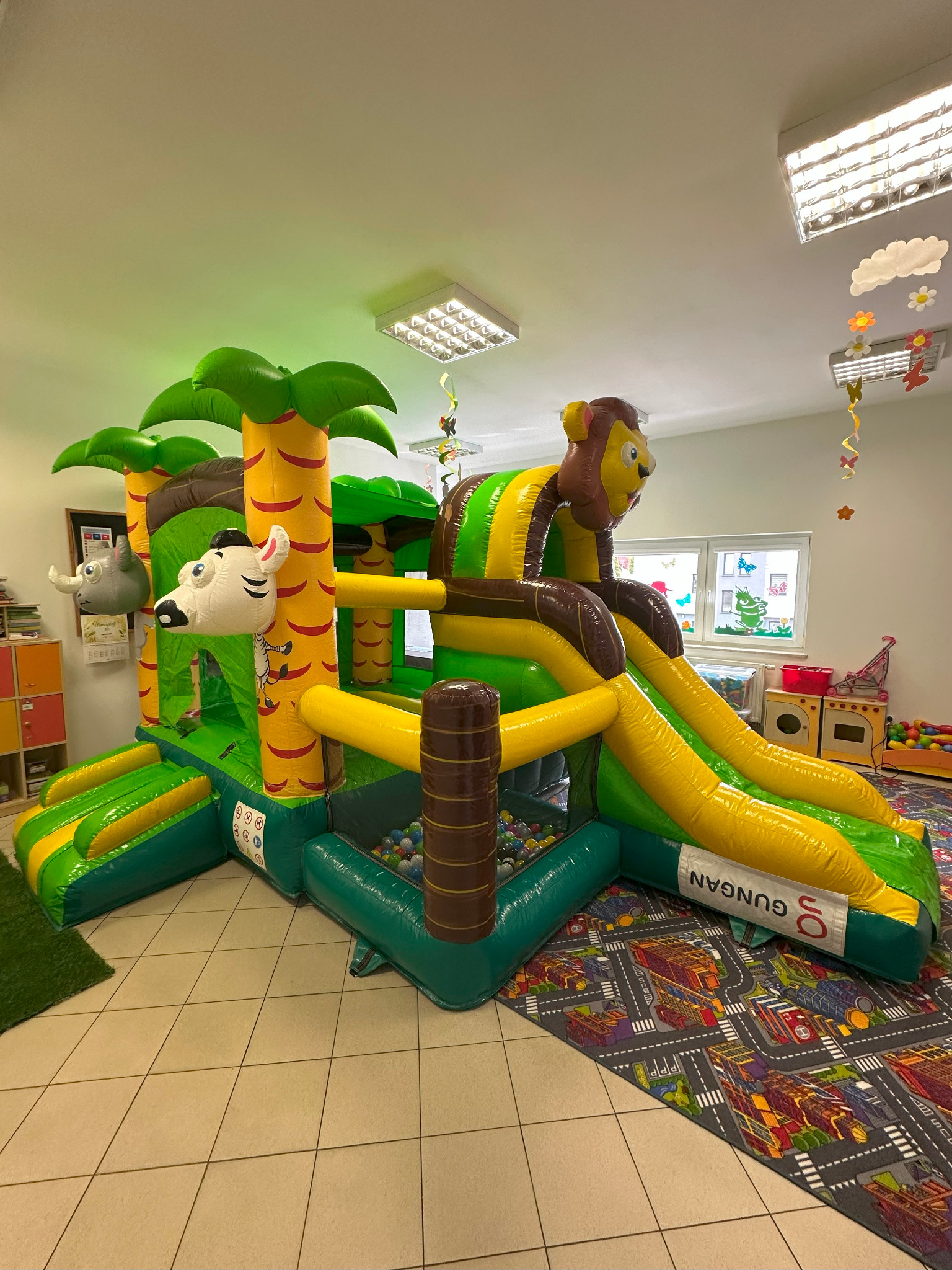 Kolorowy dmuchany zamek ze zjeżdżalnią w kształcie dżungli z motywem zwierząt, ustawiony w jasnym pomieszczeniu z dekoracjami.