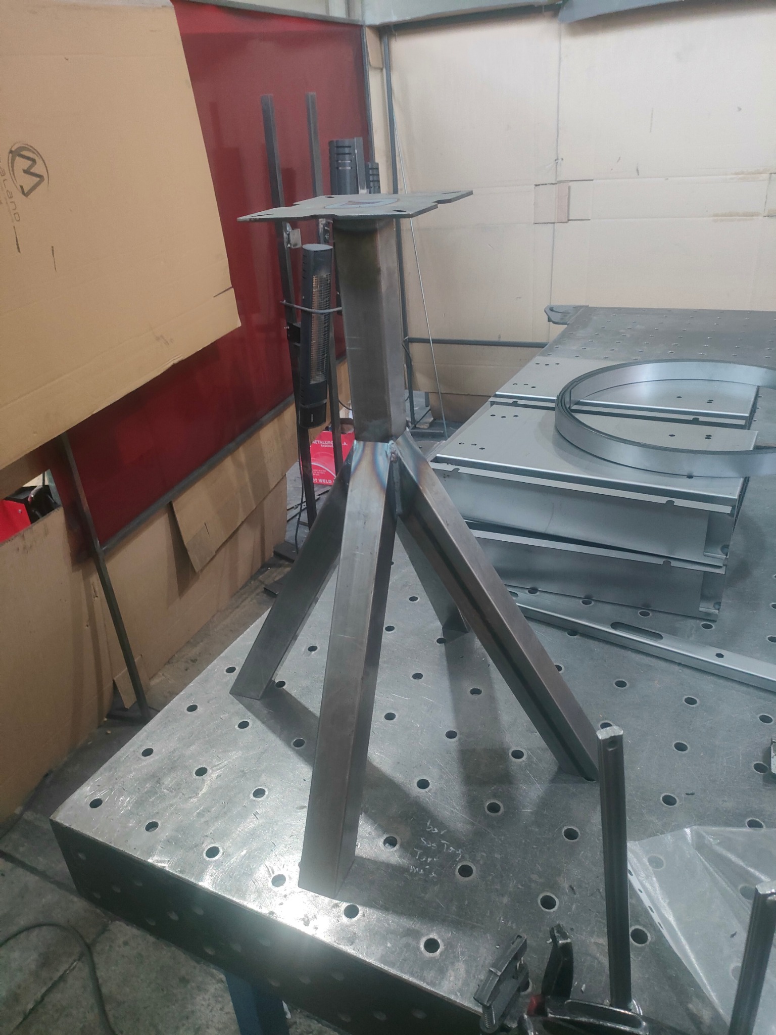 Metalowa konstrukcja stołu spawalniczego w trakcie tworzenia; widoczne spawy i elementy mocujące na perforowanym stole warsztatowym.