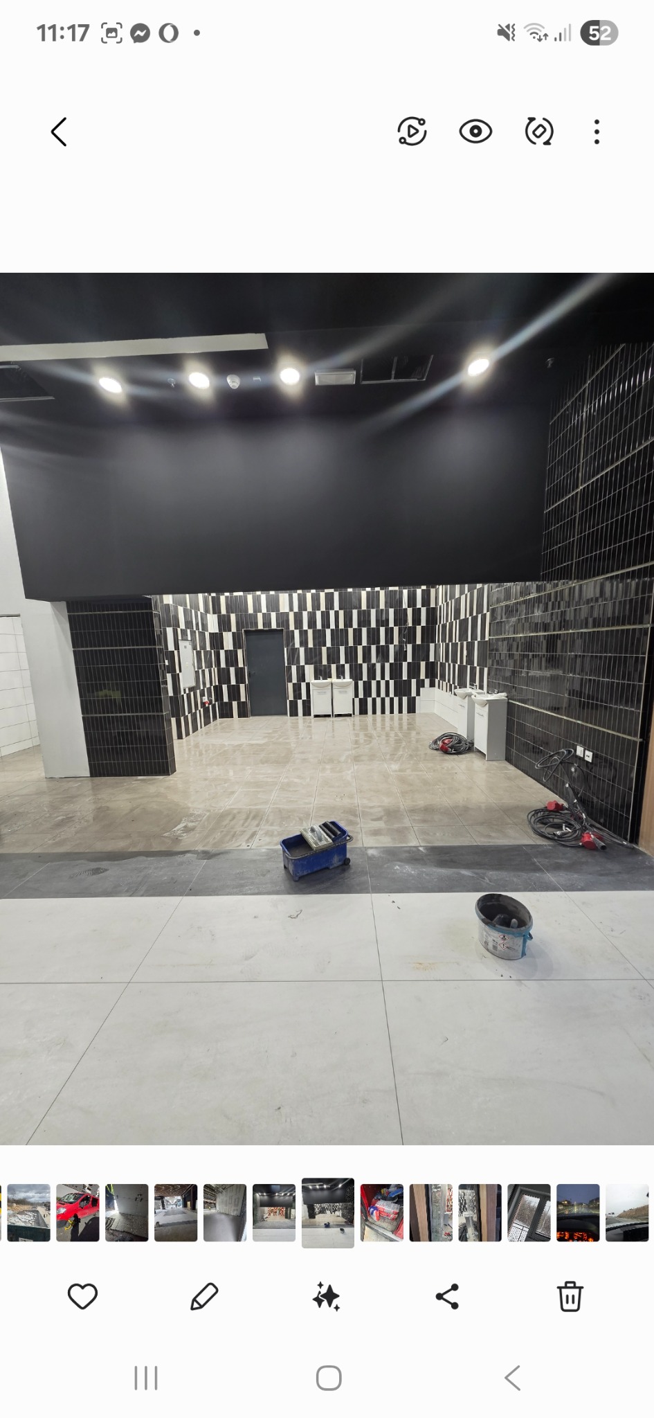 Wykończona łazienka z czarno-białymi płytkami na ścianach i jasnymi płytkami na podłodze. Widoczne narzędzia glazurnicze. Całość w nowoczesnym stylu.