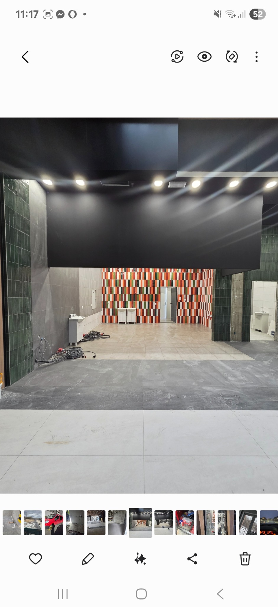 Wnętrze komercyjne w trakcie wykańczania: położona częściowo podłoga z płytek, ściany z mozaiką w odcieniach czerwieni, zieleni i bieli. Widoczne niedokończone instalacje.